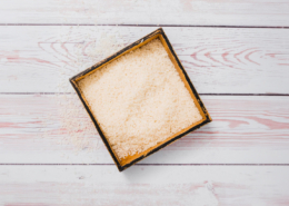 Top view of loose vermiculite granules in a square wooden tray on a light wooden surface.